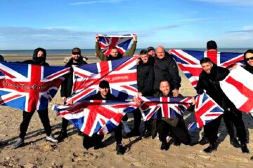 Small group waving flags on a French beach near Calais with police nearby