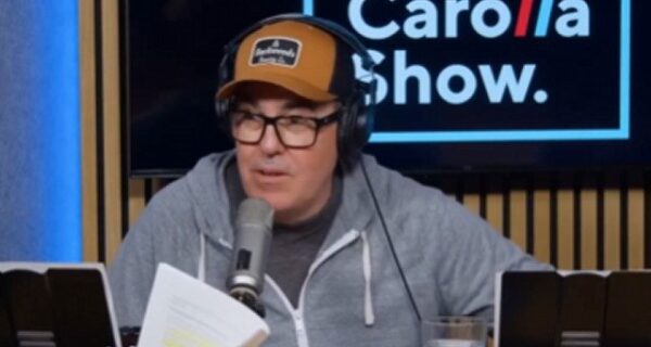 Adam Carolla speaking into a microphone during a podcast