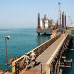 Oil rigs silhouetted against a fiery sky representing rising oil prices