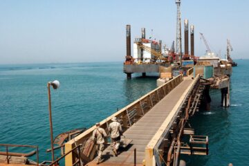 Oil rigs silhouetted against a fiery sky representing rising oil prices