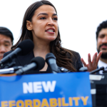 Alexandria Ocasio-Cortez speaking at a rally in Alabama behind bulletproof glass