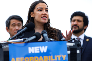 Alexandria Ocasio-Cortez speaking at a rally in Alabama behind bulletproof glass