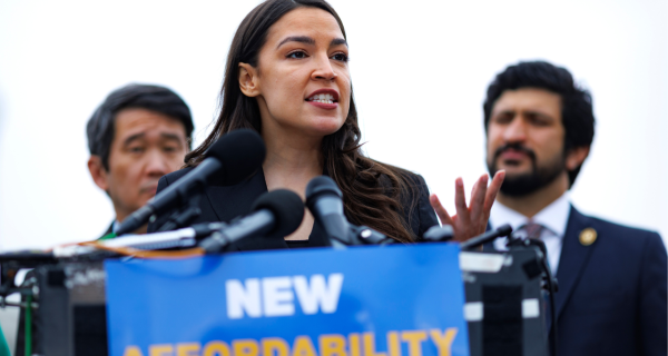 Alexandria Ocasio-Cortez speaking at a rally in Alabama behind bulletproof glass