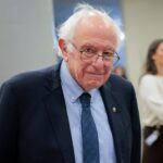 Bernie Sanders speaking at a campaign event with a Netflix logo nearby