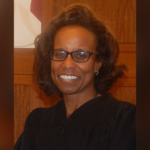 Federal judge ruling on an election case with a voting sign in the background