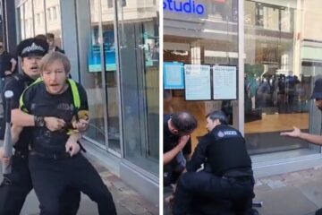 British police officers detain a man carrying a baseball bat still in its store packaging as bystanders protest