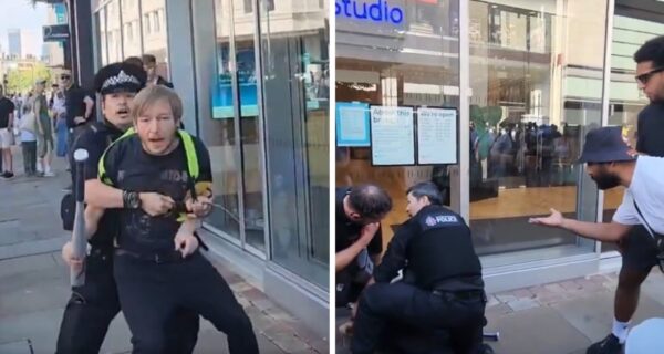 British police officers detain a man carrying a baseball bat still in its store packaging as bystanders protest